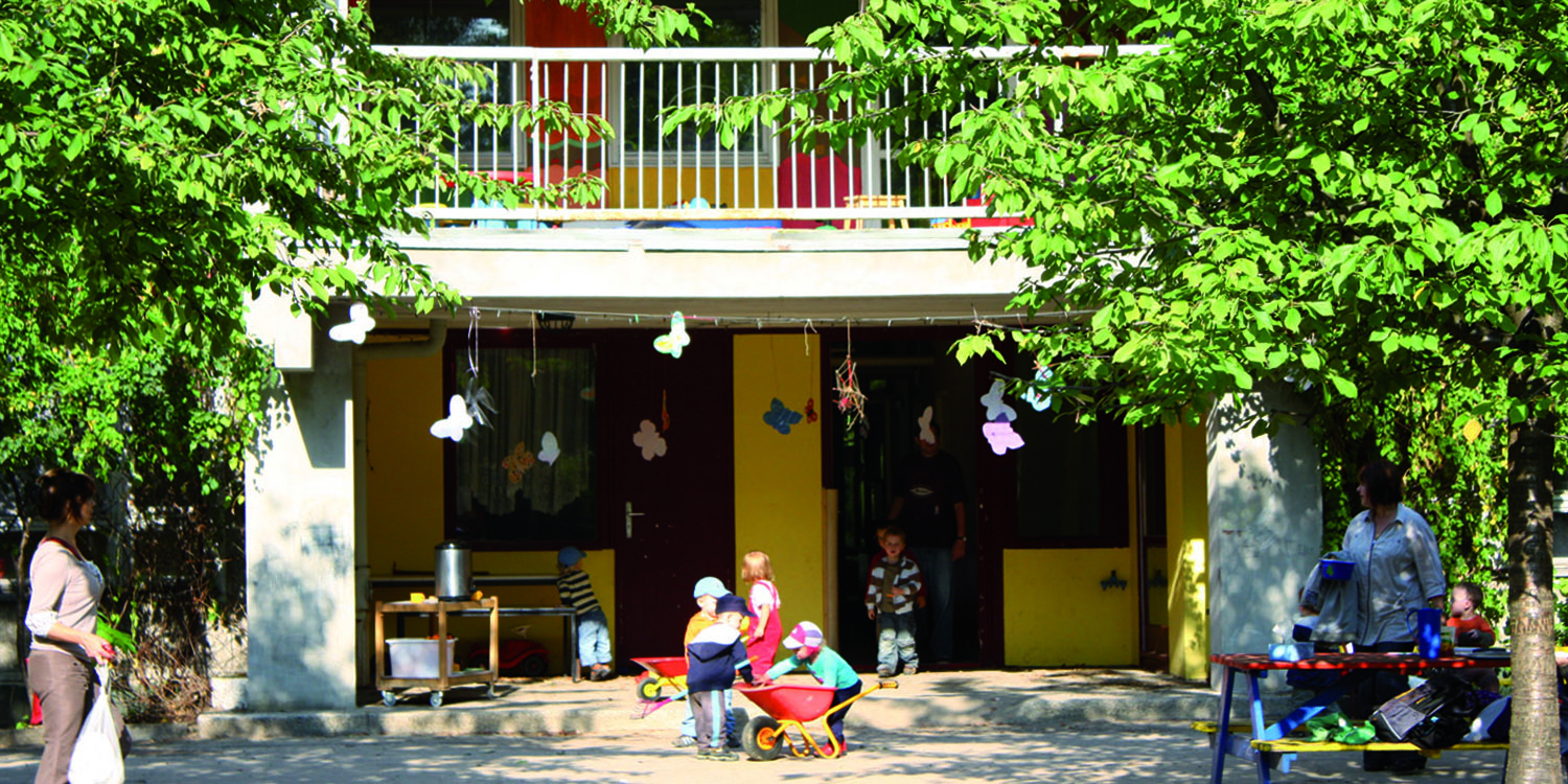 Geschmückte Hausfassade und mehrere Kinder die mit Schubkarren spielen