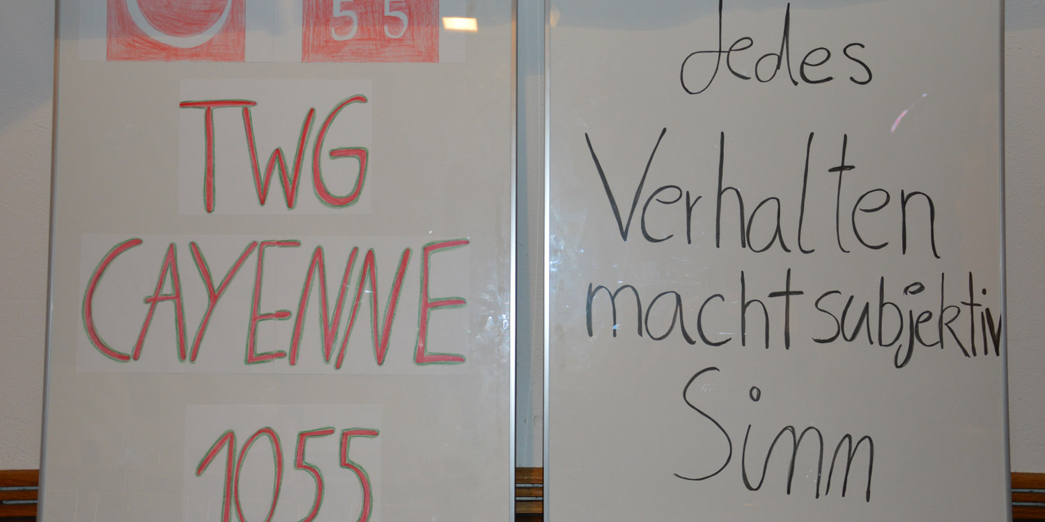 Zwei Whiteboards nebeneinander, dass eine hat das Logo und die Aufschrift "twg cayenne 1055" und auf dem anderen steht " Jedes Verhalten macht subjektiv Sinn"