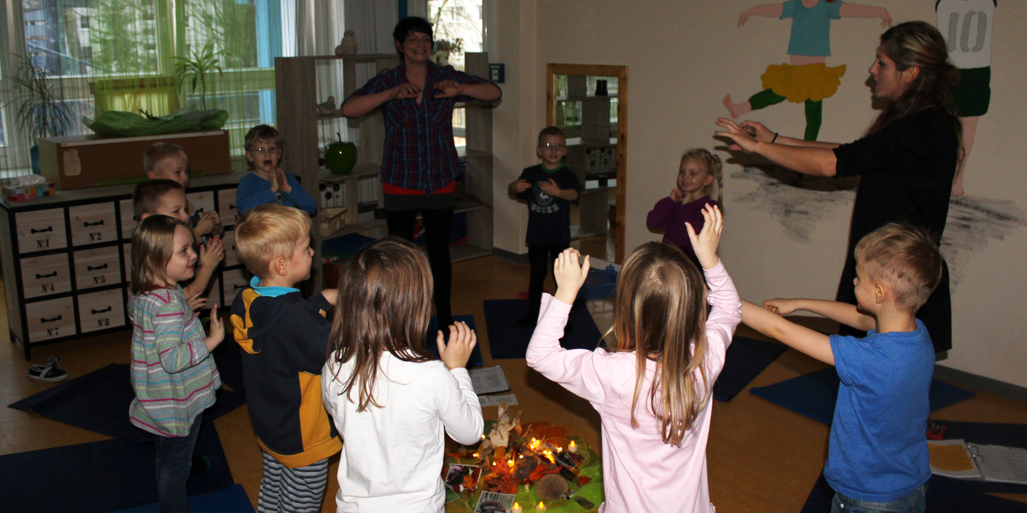 Mehrere Kinder und Erzieher stehen in einem Kreis und machen Bewegungen