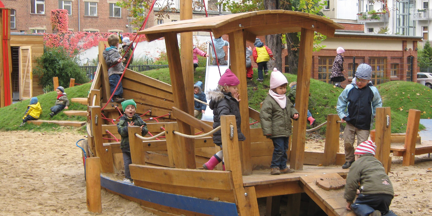 Viele Kinder spielen auf einem Spielplatz und sind auf einem Holzgerüst, das aussieht wie ein Boot