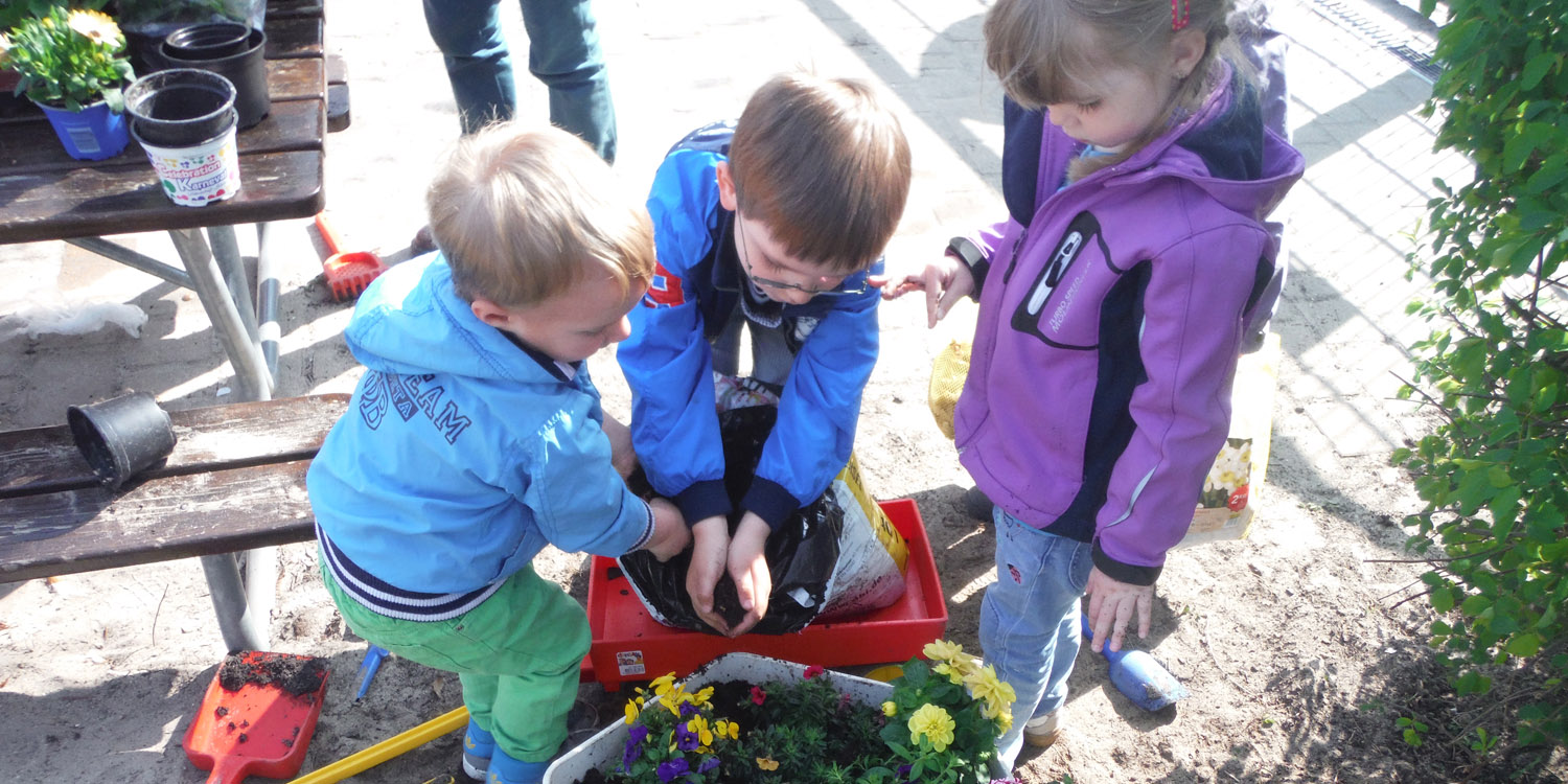 Kinder schütten Erde aus einem Sack in einem Blumentopf