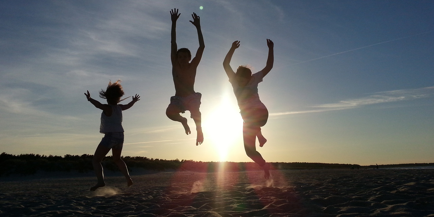 Drei junge Menschen springen am Strand bei einem Sonnenuntergang in die Luft.