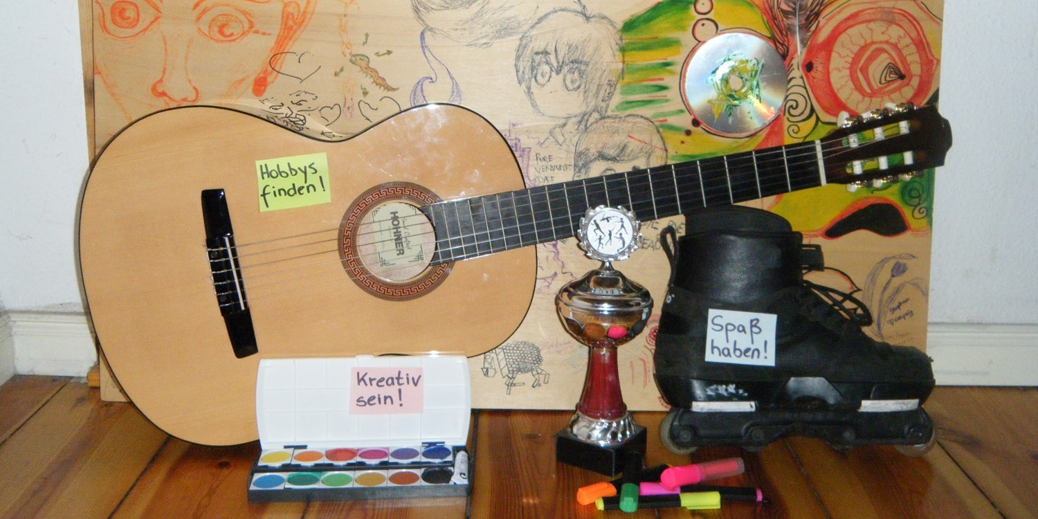 Mehrere Gegenstände, wie zum Beispiel ein Pokal, eine Gitarre oder ein Tuschkasten, stehen auf einem Schrank