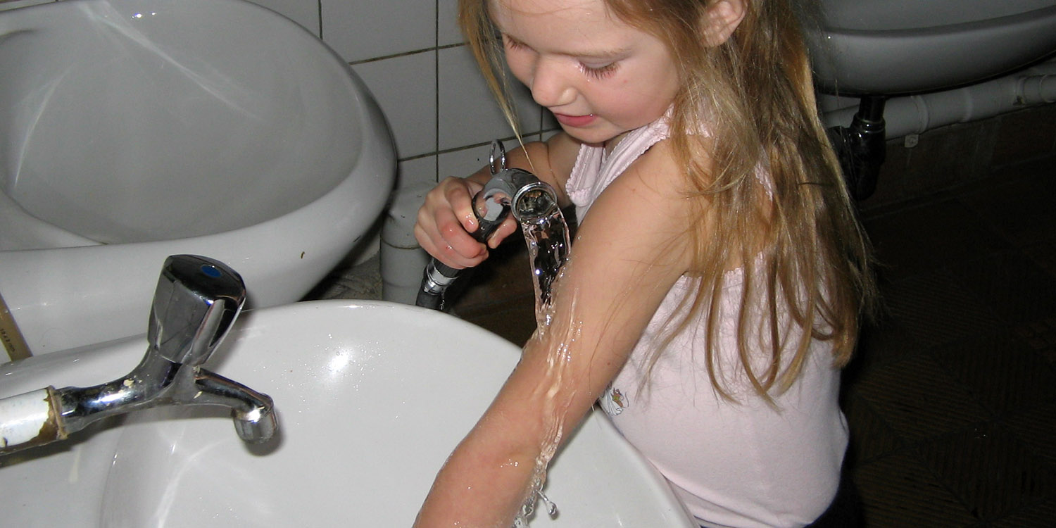 Mädchen wäscht sich mit einem Schlauch an einem Waschbecken den Arm