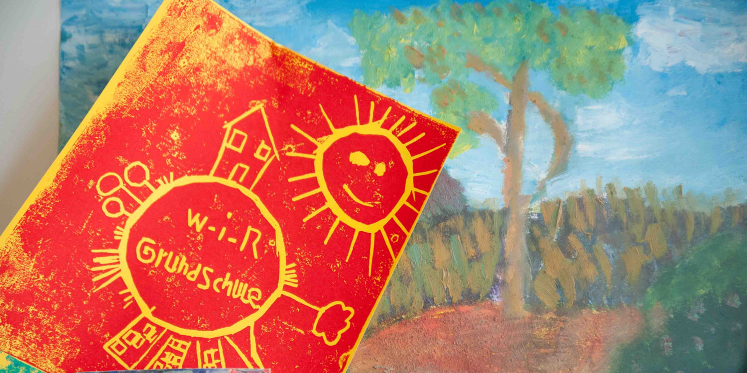 Zwei Bilder, das eine hat einen Schriftzug mit W-I-R Grundschule und wird von einem Kreis umhüllt, der die Erde darstellen sollen, mit einer Sonne und das zweite Bild ist ein Baum