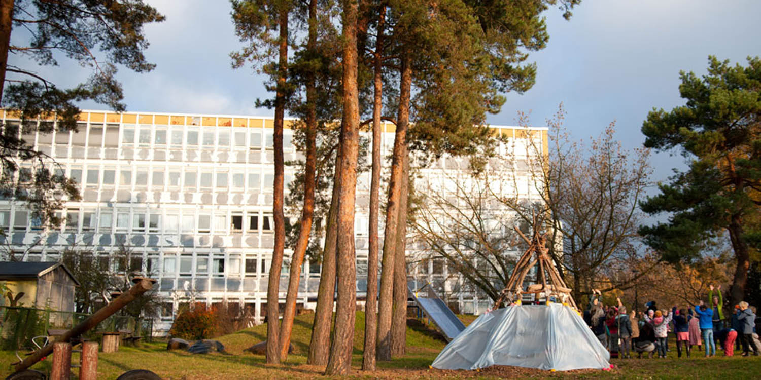 Im Hintergrund ist das Schulgebäude und im Vordergrund ist ein Spielplatz