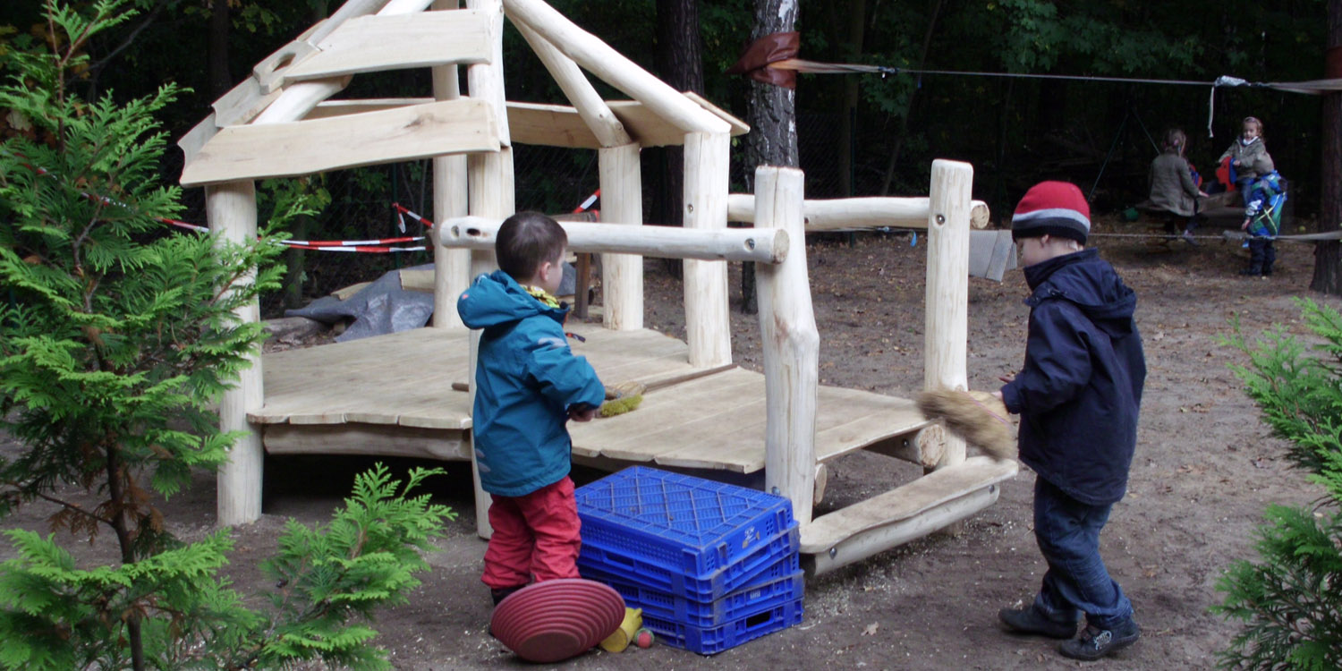 Zwei Kinder stehen vor einer kleinen Holzhütte und haben etwas in der Hand