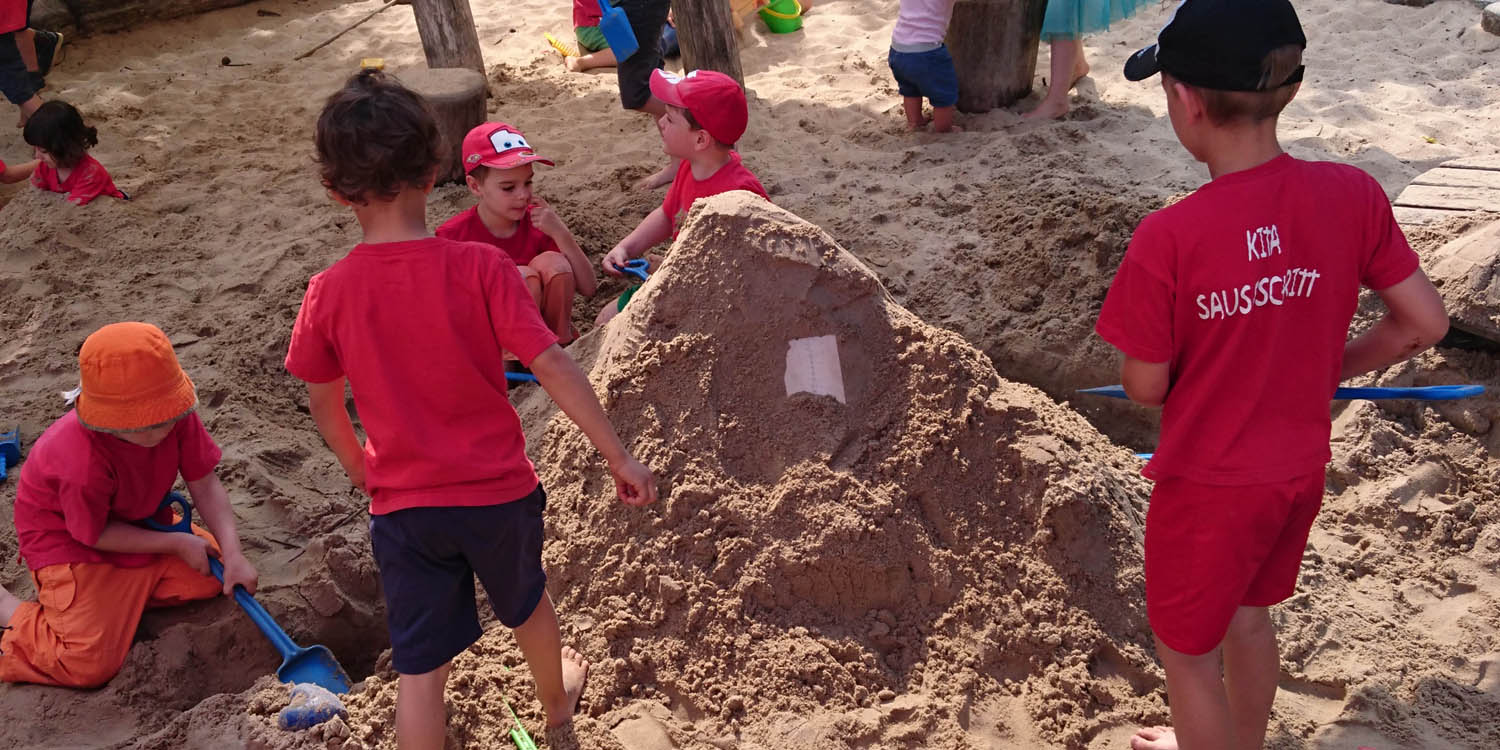 Ein Sandkasten in dem Kinder einen Berg aus Sand aufschaufeln