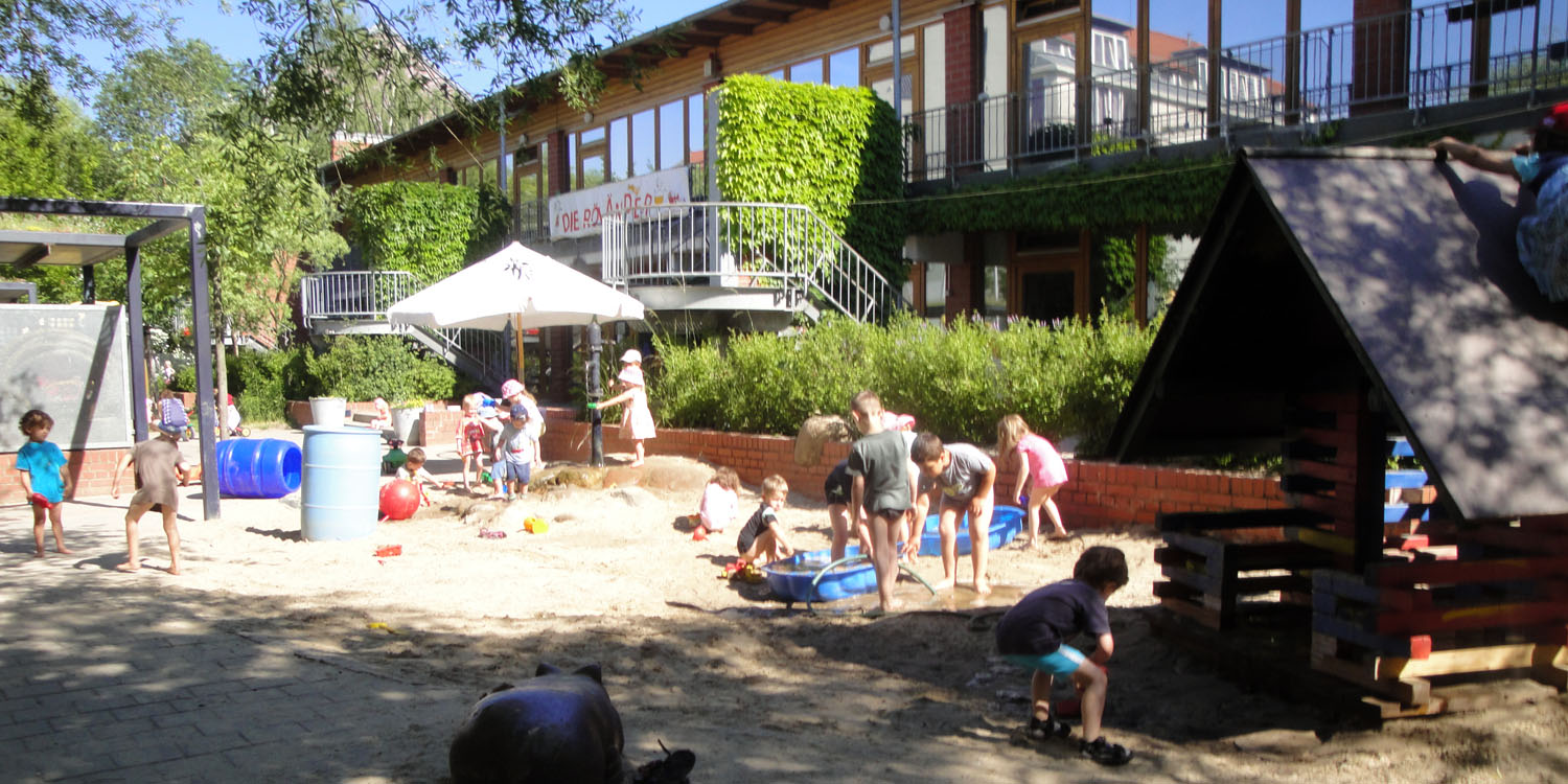 Viele Kinder die auf dem Sandspielplatz der Kita spielen