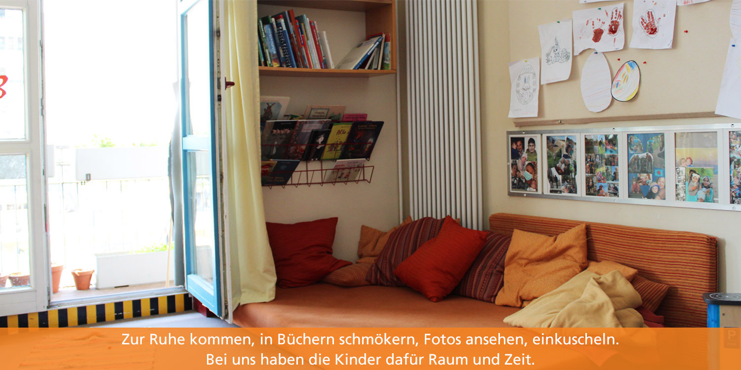 In der Ecke des Gruppenraumes liegt eine Matratze, auf der die Kinder entspannnen, lesen und sich ausruhen können. An der Wand hängt eine Regal mkit Büchern. Das Fenster ist geöffnet und lässt Tageslicht hineinstömen.