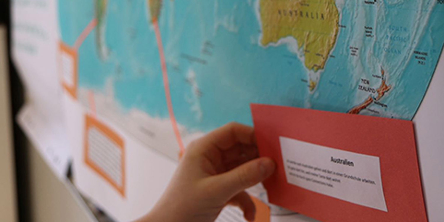 Ein Schüler kleibt eine Karteikarte mit Informationen über Australien an eine große Weltkarte unter den Kontinent.