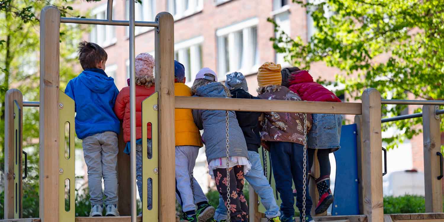 Sieben Kinder stehen auf einem Holzklettergerüstund sehen interessiert nach unten.