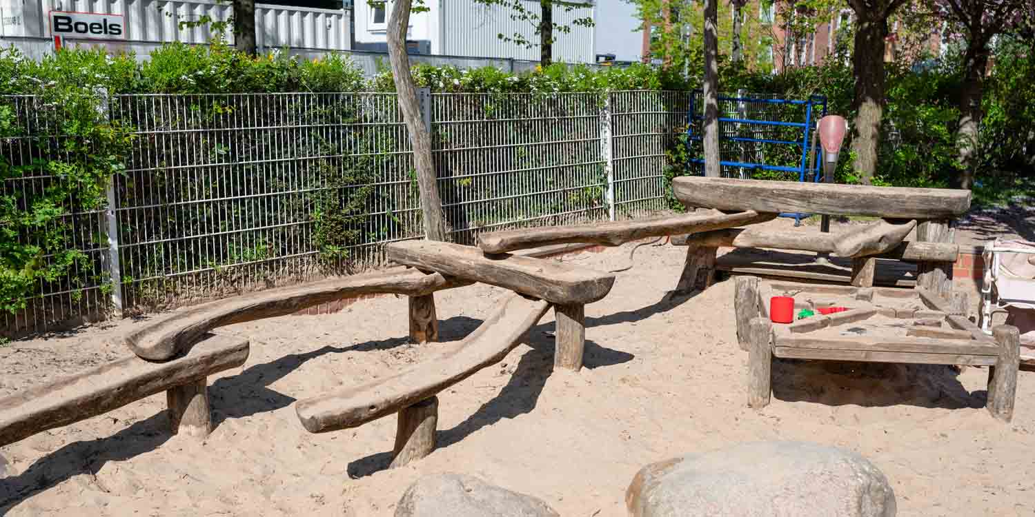 Auf der Freifläche der Kita steht eine Wasserspieleanlage mit mehreren ausgehöhlten Baumstämmen. Große Steine laden zum Klettern ein.