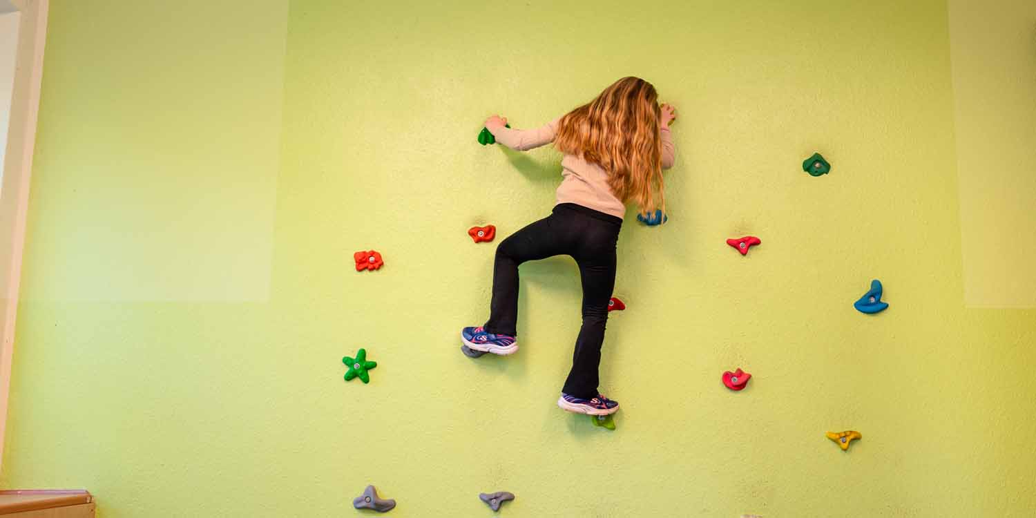 Ein Mädchen klettert eine Kletterwand in der Kita hoch.