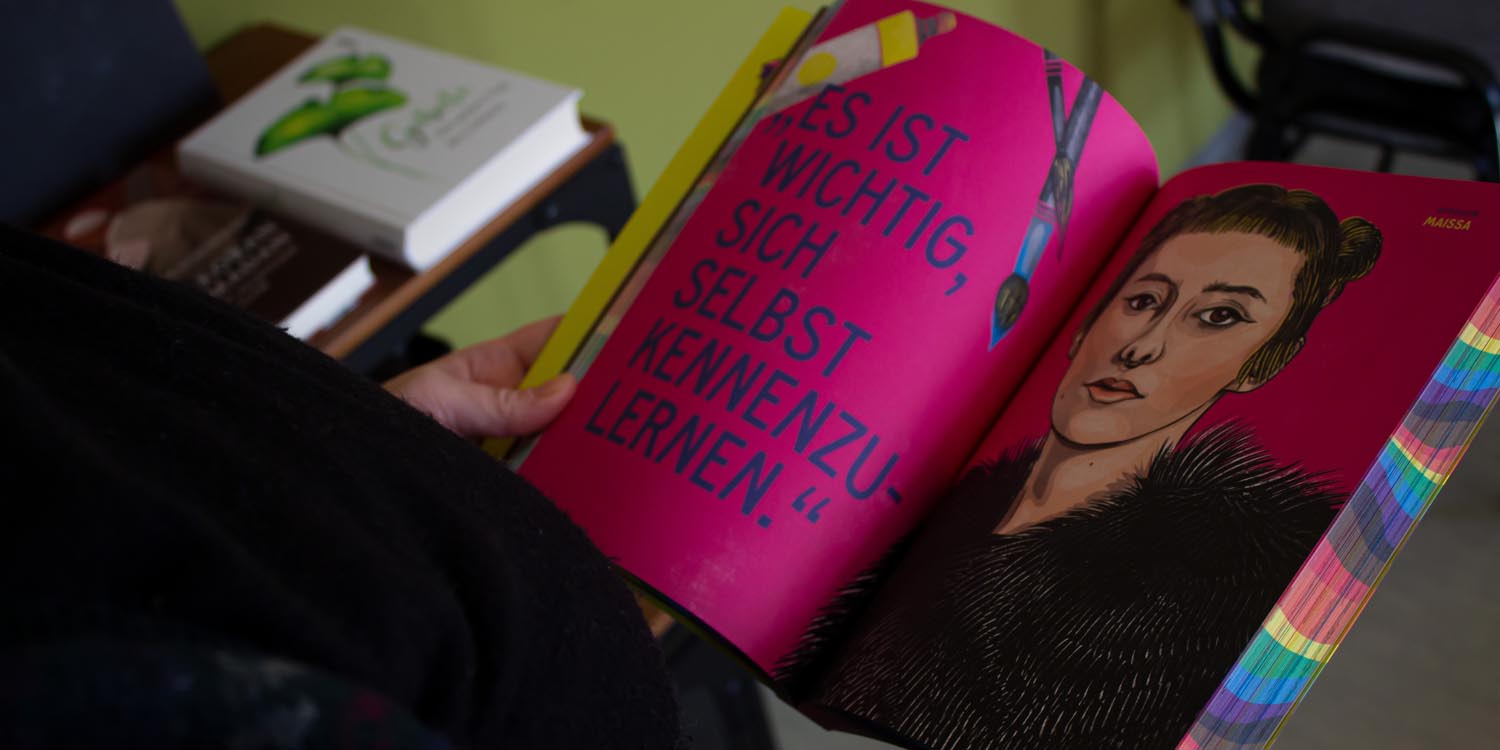 Ein junger Mensche blättert in einem Buch und hat eine pinkfarbene Seite vor sich, auf der steht: "Es ist wichtig, sich selbst kennenzulernen." auf der rechten Seite ist das Bidnis einer Frau.