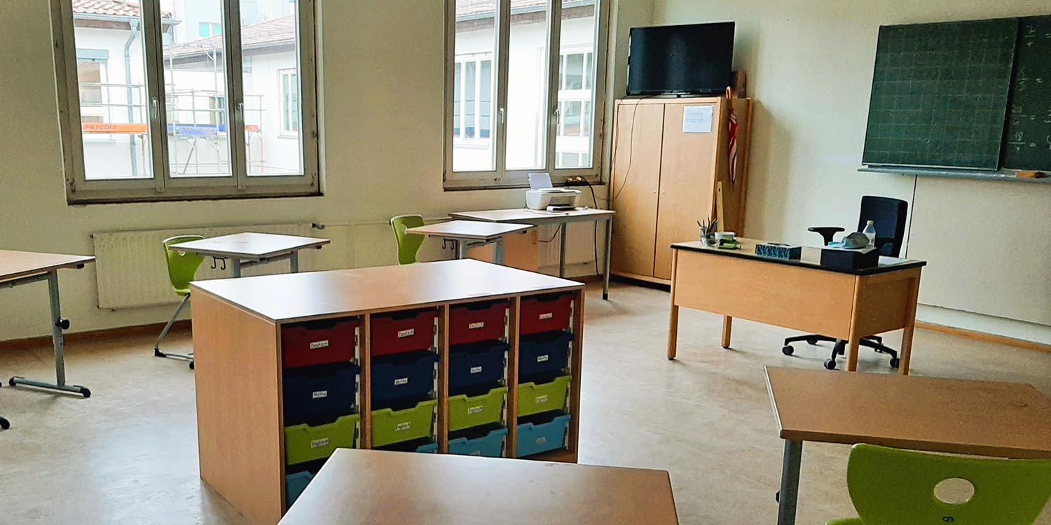 In einem Klassenraum stehen Tische, Regale und Stühle in loser Anordnung.