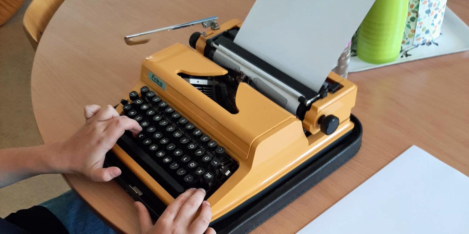 Eine Schülerin oder ein Schüler schreibt einen Text auf einer alten Schreibmaschine.