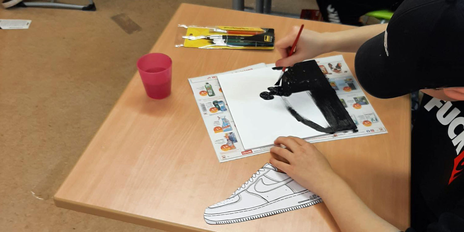 Ein Schüler zeichnet einen Turnschuh auf ein Blatt Papier.