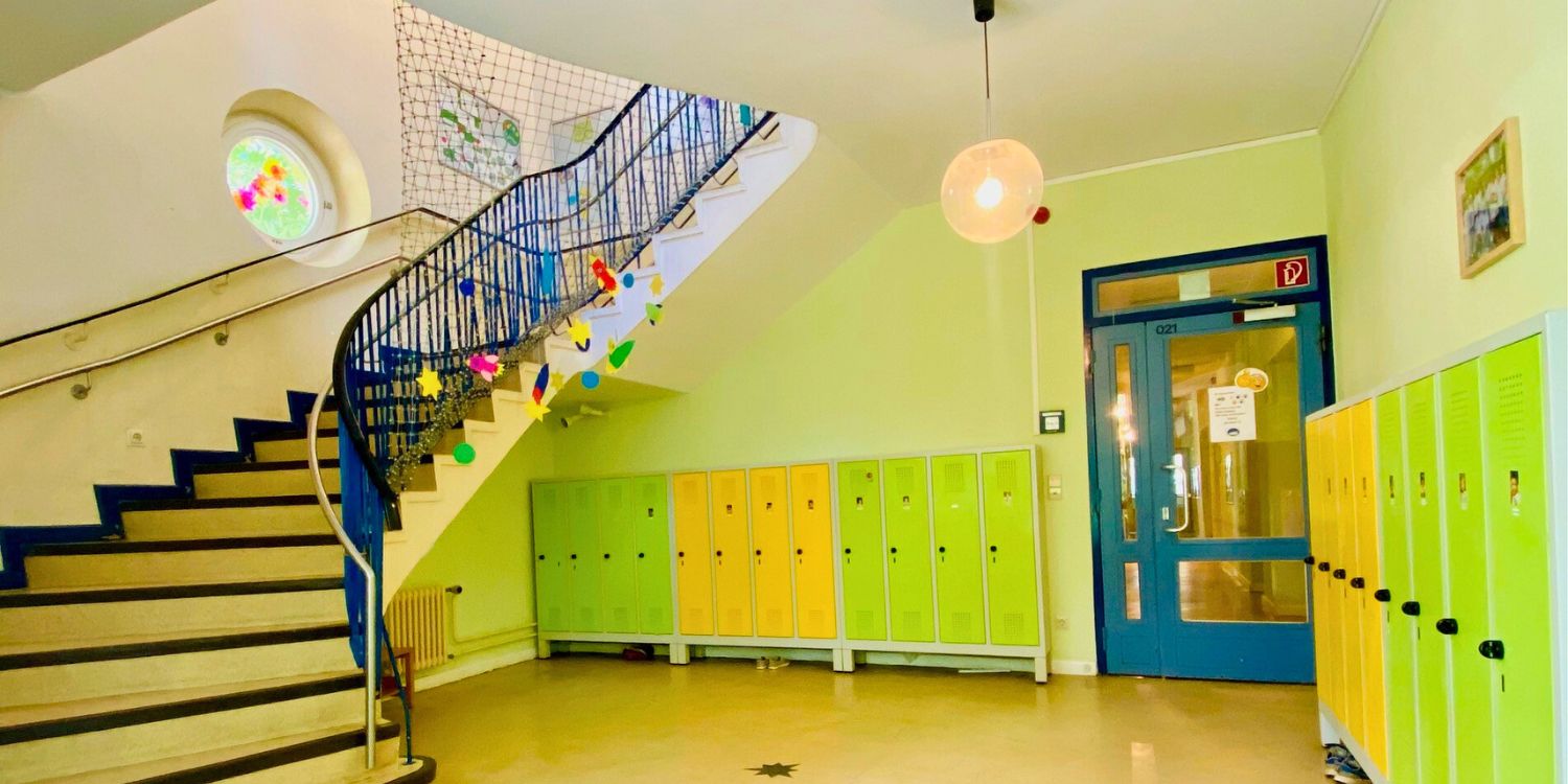 Eine Treppe führt von der Gardeobe mit grünen und gelben Schränkchen in das obere Stockwerk.