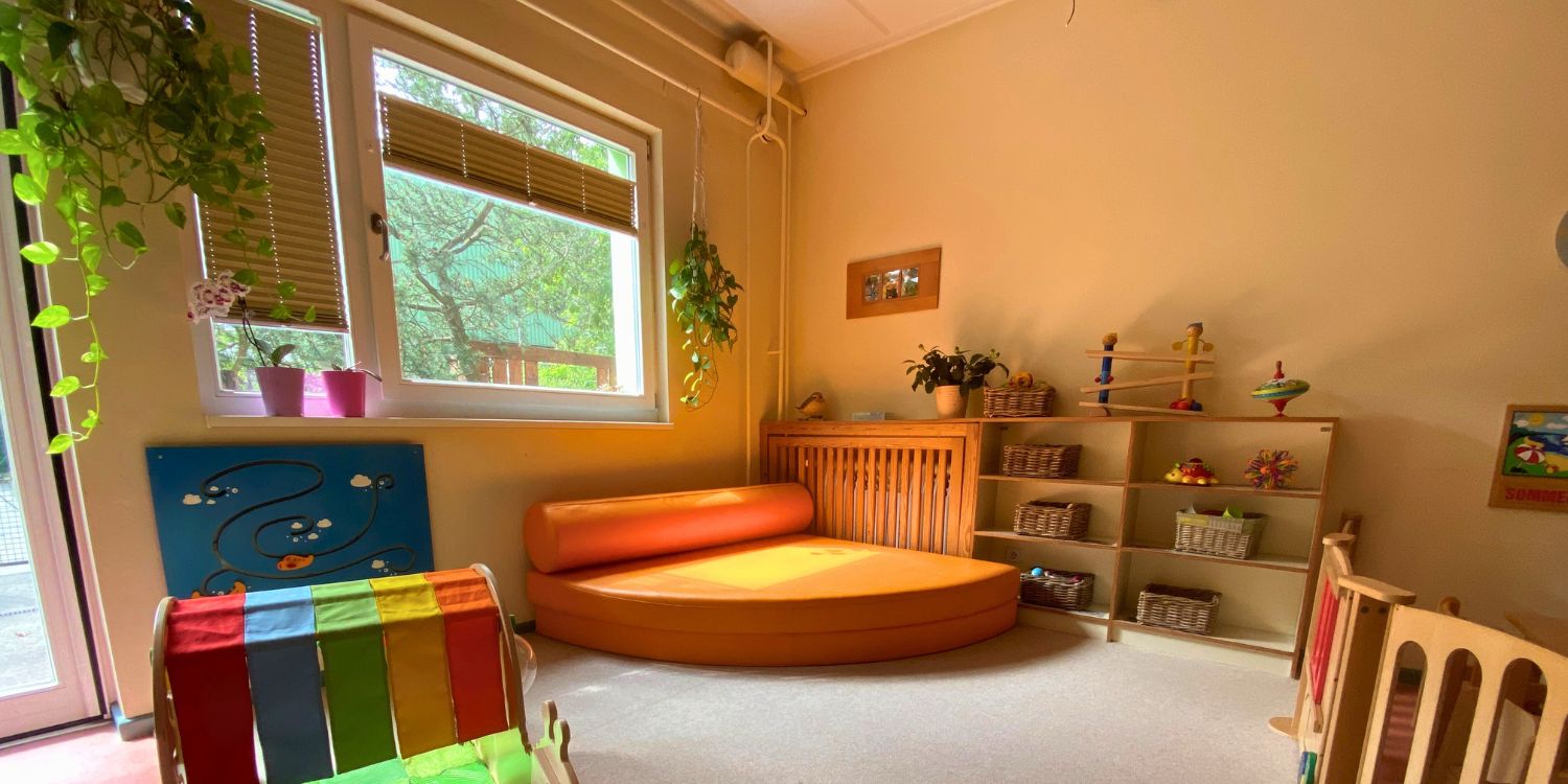 In der Ecke eines Raume steht eine halbrunde Couch zum Entspannen. An der Seite stehen Regale mit Bastelmateralien.