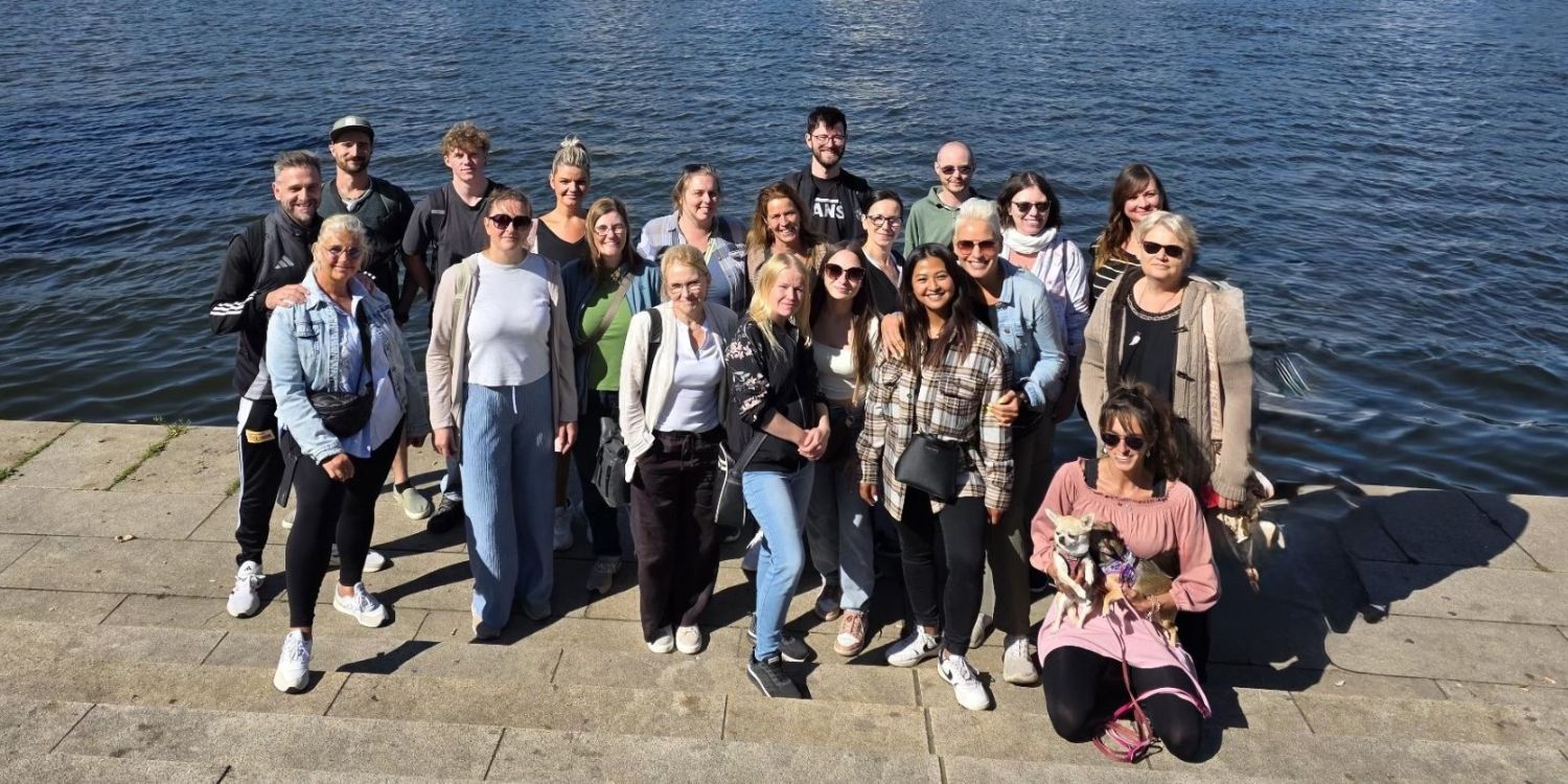 21 Personen stehen am Ufer eines Flusses und lächeln in die Kamera.