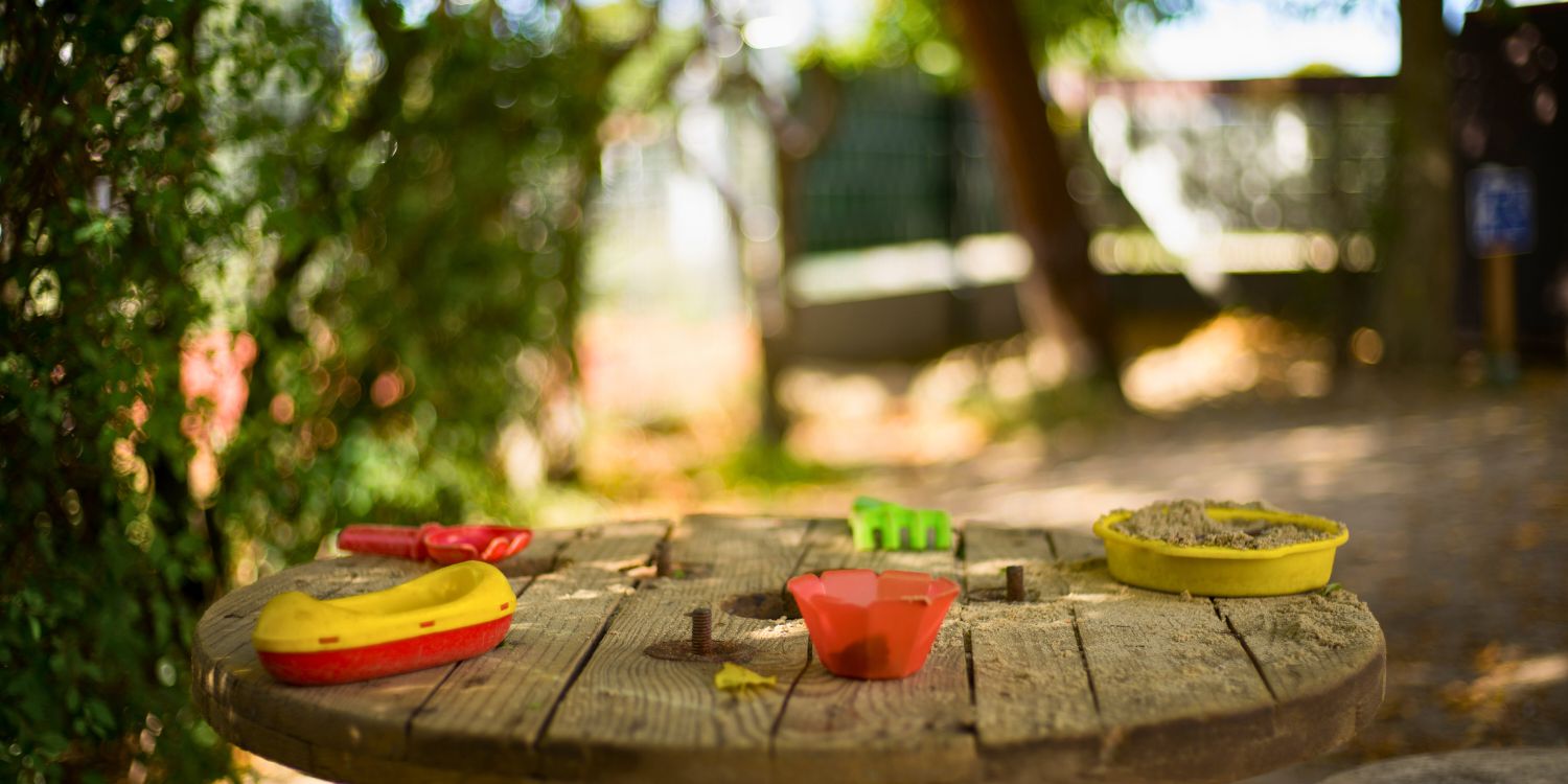 Auf einem runden Holztisch im Garten stehen kleine Sandformen.
