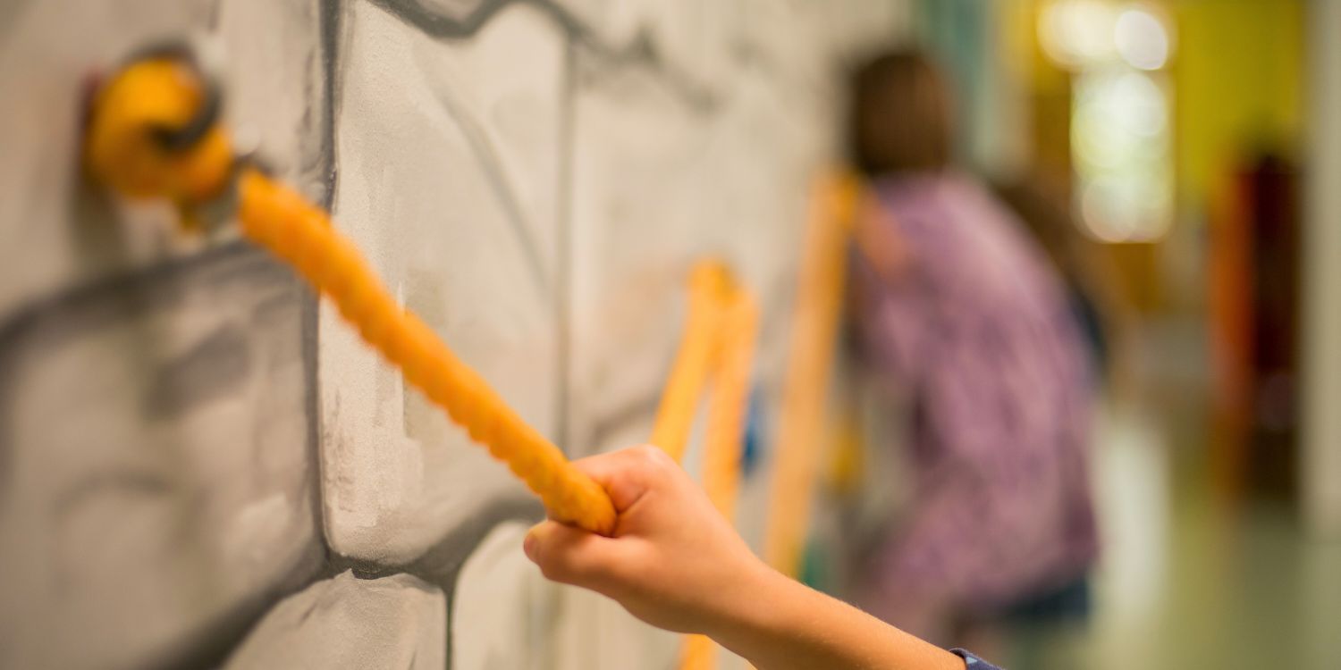 Kinderhand greift nach Seil an Kletterwand