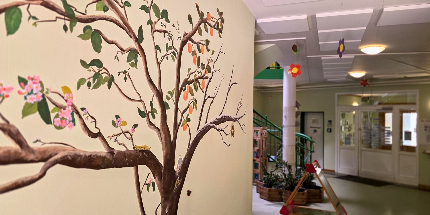 Links ein Wand mit einem aufgemalten bunten Baum; der Blick führt in den Flur.