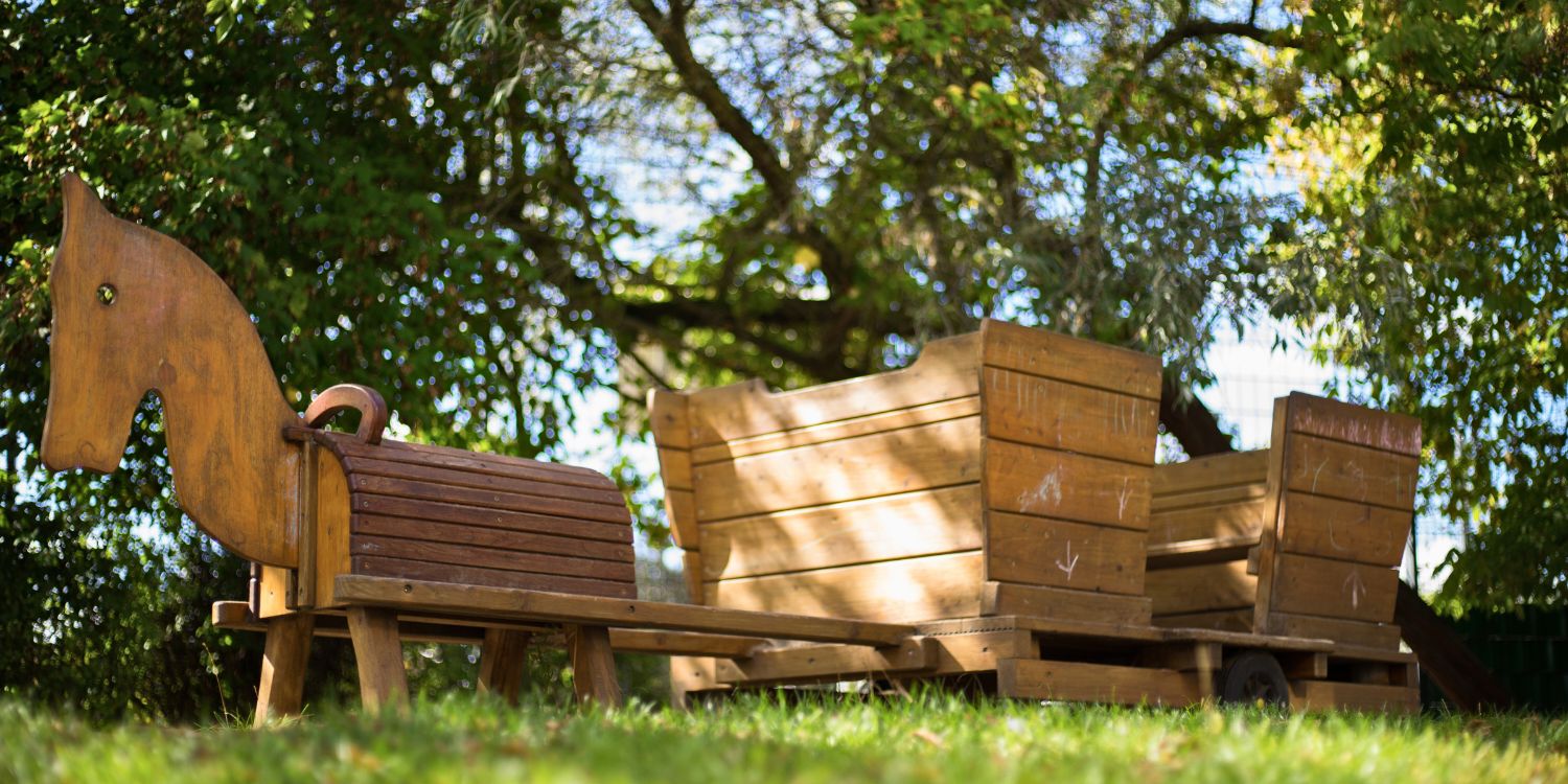 Ein Holzpferd zieht einen Holzwagen im Garten.